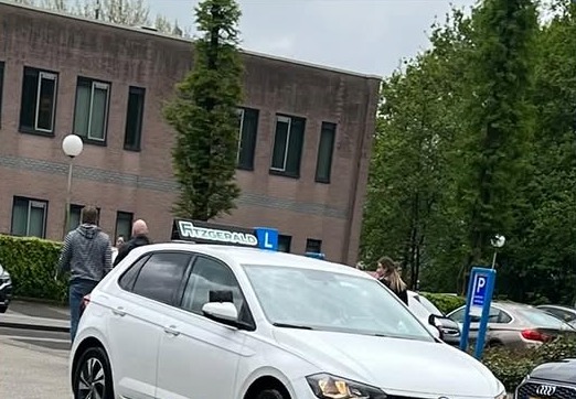 De lesauto van Rijschool Fitzgerald: een witte Volkswagen Polo met het Fitzgerald-dakbord